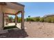 Landscaped backyard with covered patio, desert rock ground cover, and lush perimeter vegetation at 15874 W Wildflower Dr, Surprise, AZ 85374