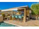 Outdoor kitchen with bar seating, BBQ, and tv, next to a swimming pool and desert landscape at 11796 W Creosote Dr, Peoria, AZ 85383