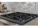 A modern kitchen stove top with blue flames and grey backsplash at 11796 W Creosote Dr, Peoria, AZ 85383