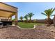 Backyard featuring lush green lawn, palm trees, rock accents, and covered patio at 41448 N Eliana Dr, Queen Creek, AZ 85140