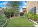 Landscaped backyard with synthetic grass bordered with leafy bushes, palm trees, and a tall tree at 4615 E Navigator Ln, Phoenix, AZ 85050