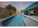 Backyard pool featuring clean blue water, a Baja shelf, lush greenery, and a shaded patio lounge area at dusk at 16368 W Cortez St, Surprise, AZ 85388