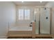 Bright bathroom featuring a soaking tub beneath shuttered windows and a glass-enclosed shower at 40759 W Bravo Dr, Maricopa, AZ 85138