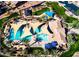 Aerial view of a community pool with shade structures, lounge chairs, palm trees, and colorful playground equipment nearby at 1101 W Oleander Ave, Queen Creek, AZ 85140