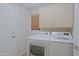 Bright laundry room featuring a full washer and dryer set, wooden blinds, and upper cabinet storage space at 42812 W Venture Rd, Maricopa, AZ 85138