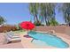 Beautiful backyard pool with waterfall feature, red umbrella, and lounge chairs perfect for relaxing at 42812 W Venture Rd, Maricopa, AZ 85138