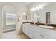 Bathroom featuring dual sinks, white cabinetry, marble countertops, arched mirror, and step-in shower at 18819 N 49Th Ave, Glendale, AZ 85308