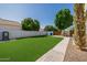 Spacious backyard with lush artificial turf, a paved walkway, and mature trees, providing a low-maintenance outdoor space at 3955 E Fox Cir, Mesa, AZ 85205