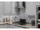 Close-up of a gas stove with decorative tile backsplash, a stainless steel hood, and white cabinets at 3955 E Fox Cir, Mesa, AZ 85205