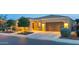 Well-maintained home exterior featuring a two-car garage, manicured landscaping, and warm exterior lighting at 1673 E Laddoos Ave, Queen Creek, AZ 85140