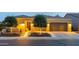 Inviting home exterior featuring warm lighting, a well-manicured lawn, and an attached two-car garage at dusk at 1673 E Laddoos Ave, Queen Creek, AZ 85140