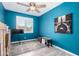 Bedroom with wood-look tile flooring, ceiling fan, window with white blinds, and modern art against the blue wall at 40913 W Williams Way, Maricopa, AZ 85138