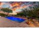 Sparkling swimming pool with integrated water features, framed by lush landscaping and a mesmerizing sunset at 10119 E Winter Sun Dr, Scottsdale, AZ 85262