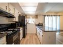 Kitchen features white cabinets, black appliances, wood floors and countertop bar with granite countertop at 6337 N 49Th Ave, Glendale, AZ 85301