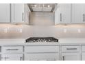 A modern kitchen features white cabinetry and a gas cooktop with a decorative tile backsplash at 17632 W Oregon Ave, Litchfield Park, AZ 85340