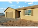 A single-story tan home with a brown roof, brown shutters, and a two-car garage under a cloudy blue sky at 31824 N 221St Dr, Wittmann, AZ 85361