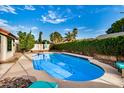 An inground kidney shaped pool features a new pool cleaner and is surrounded by mature landscaping at 11035 E Clinton St, Scottsdale, AZ 85259