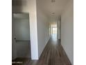 An open hallway featuring stylish wood-look floors, white walls, and access to other rooms in the home at 46963 W Coe St, Maricopa, AZ 85139