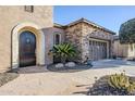 Inviting entryway with stone walkway leading to an arched doorway and a stone accented garage at 27587 N Makena Pl, Peoria, AZ 85383