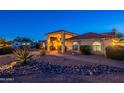 Desert landscape with rock mulch and a covered entry with a red tile roof illuminated in the evening at 13108 N 76Th St, Scottsdale, AZ 85260