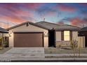 A single story home with a two-car garage, stone accents and a beautiful sunset at 16032 W Desert Hollow Dr, Surprise, AZ 85387