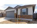 Single-Gathering home featuring stone accents, a gray garage door, desert landscaping, and a young tree at 8584 N 170Th Ln, Waddell, AZ 85355