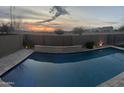 Stunning sunset view from a backyard pool with a stone wall and modern landscaping at 22898 N 94Th Ln, Peoria, AZ 85383