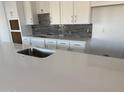 Modern kitchen features sleek white cabinets, gray backsplash, and stylish countertops with stainless steel sink at 31277 N 130Th Ave, Peoria, AZ 85383
