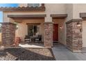 Covered porch with stone columns, two wicker chairs, and a red door at 14570 N 142Nd Ln, Surprise, AZ 85379