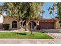 Tan stucco house with brown garage door, lush lawn, and mature trees at 10473 N 87Th Pl, Scottsdale, AZ 85258