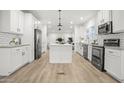 White kitchen with island, stainless steel appliances, and light wood flooring at 2693 S 357Th Dr, Tonopah, AZ 85354