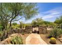 Backyard gate with stone surround and metal design leading to landscaped desert scenery with mature native trees at 10567 E Mark Ln, Scottsdale, AZ 85262