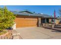 Front view of a single story home with a wooden garage door and mature trees at 5210 W Ironwood Dr, Glendale, AZ 85302