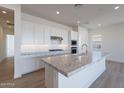 Bright kitchen with white cabinetry, stainless steel appliances, and an island with marble countertops at 3752 W Antelope Way, San Tan Valley, AZ 85144