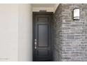 Contemporary front door with stone accents and modern light fixture, creating a welcoming entry at 27256 N 74Th Ln, Peoria, AZ 85383