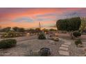 Landscaped backyard with fire pit, stone pathway, and desert plants at sunset at 23187 W Lasso Ln, Buckeye, AZ 85326