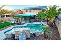 Backyard oasis featuring a sparkling pool, lush landscaping, and covered patio with solar panels at 15727 W Rimrock St, Surprise, AZ 85374