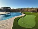 Backyard featuring a pool, putting green, artificial grass, and desert landscaping at 9900 E Desert Trail Ln, Gold Canyon, AZ 85118