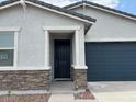 Close-up of front door with stone accents, a dark-blue garage door, and manicured landscape at 17457 W Eva St, Waddell, AZ 85355