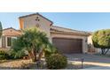 Tan house with a 2-car garage and lush landscaping in the front yard at 21720 N 265Th Dr, Buckeye, AZ 85396