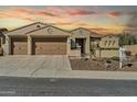 Inviting home featuring a 3-car garage, desert landscaping, and classic Southwestern architecture at sunset at 30696 N 130Th Ln, Peoria, AZ 85383