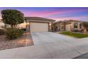 Charming single-story home with a spacious driveway, desert landscaping, and warm exterior lighting at dusk at 7815 W Cinder Brook Way, Florence, AZ 85132