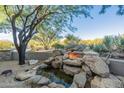 Relaxing backyard with a rock waterfall, fire feature, and lush desert landscaping for a serene outdoor experience at 37870 N 98Th Pl, Scottsdale, AZ 85262
