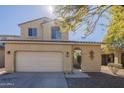 Two-story tan home with an attached garage, desert landscaping, and a sunny view at 10423 W Hughes Dr, Tolleson, AZ 85353