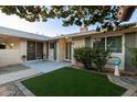 Charming front yard featuring low maintenance synthetic grass, lush tree with greenery, and an inviting patio area at 10808 W Kelso Dr, Sun City, AZ 85351
