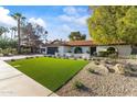 A stylish home with an expansive green lawn, xeriscaping, dark garage, and appealing curb appeal at 7607 E Charter Oak Rd, Scottsdale, AZ 85260