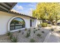 A close up of the xeriscaped front yard and unique, arched windows of this lovely home at 7607 E Charter Oak Rd, Scottsdale, AZ 85260