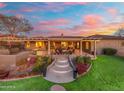 Beautiful outdoor living space with a fire pit, lush green lawn, and steps leading to a covered patio with sunset view at 27606 N 61St Pl, Scottsdale, AZ 85266