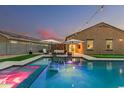 Backyard pool with built-in spa, water feature, artificial turf and lounge seating at twilight at 41954 W Plata St, Maricopa, AZ 85138