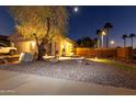 Home exterior featuring desert landscaping, mature trees, a tiered fountain, and exterior lighting for evening ambiance at 11197 W Coronado Rd, Avondale, AZ 85392